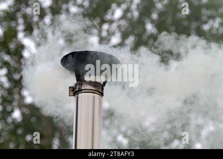 Heißer Rauch entweicht aus einer Zinnpfeife vor dem Hintergrund von Herbstbäumen Stockfoto