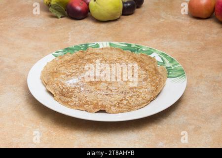 Ein weißer Teller mit grünen Blättern, belegt mit spanischen Crepes und Süßpulver, auf einer rustikalen Arbeitsplatte mit einigen Früchten in der Ba Stockfoto