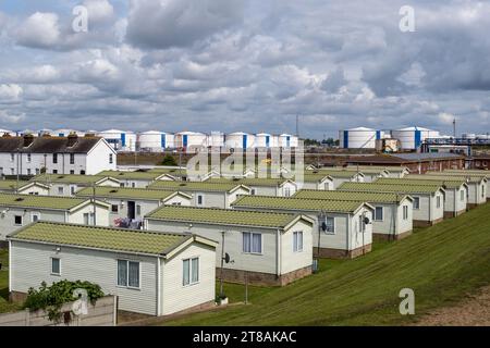 Vorgefertigte Bungalow-Häuser auf Canvey Island, Essex, mit Öltankern und flauschigen grauen Wolken im Hintergrund. England, Großbritannien, 2023. Stockfoto