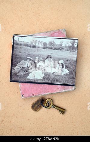 Schwarzweißdruck von 1920er Jahren englischer Arbeiterfamilie, die auf dem Feld picknickte, mit antikem Messingschlüssel und alter rosafarbener Box Stockfoto