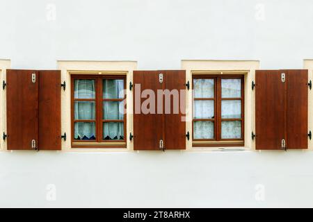 Zwei rechteckige Fenster mit braunen Rahmen und Holzläden auf weißem Hintergrund. Aus der Serie Windows of the World. Stockfoto