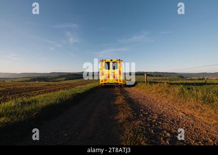 Ambulanzwagen des Notarztdienstes, der auf ländlichem Feldweg in der Mitte der Felder abfährt. Themen Dringlichkeit, Rettung und Gesundheitsfürsorge in abgelegenen Gebieten Stockfoto