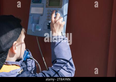 Ein Junge mit europäischem Auftritt in einer Telefonzelle spricht am Telefon. Nahaufnahme Rückansicht Alte Telefonkabine. Hochwertige Fotos Stockfoto