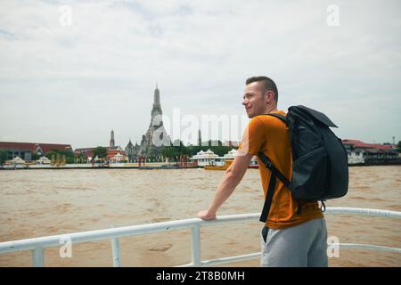 Reisende mit Rucksack genießen die Aussicht von der Fähre zum Tempel Wat Arun in Bangkok. Wunderschönes Reiseziel in Thailand. Stockfoto