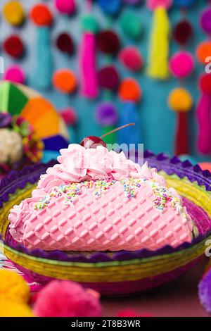 Pink Ice Cream Taco Dessert mit Sprinkles, Kirschfrucht, Schlagsahne in einem bunten handgemachten gewebten Korb auf einem festlichen Hintergrund mit Pompons Stockfoto