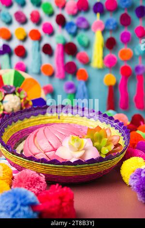 Rosafarbenes mexikanisches traditionelles Conchas-Dessert in einem farbenfrohen handgefertigten Woven-Korb mit hellen, roten, rosafarbenen, orangefarbenen und blauen Pom-Pom-Girlande und Sukkulenten Stockfoto
