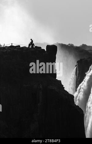 Künstlerisches Schwarzweißbild eines einsamen Grenzsoldaten auf der simbabwischen Seite der Victoria Falls, fotografiert von der sambischen Seite. Stockfoto