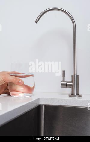 Frau bekommt gefiltertes Wasser aus rostfreiem Wasserhahn in ein Glas Stockfoto