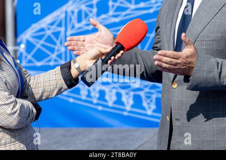 Weibliche Nachrichtenreporterin, die ein Mikrofon hält, macht ein Medieninterview mit männlichen, nicht erkennbaren Personen. VOX popoli-Konzept. Stockfoto