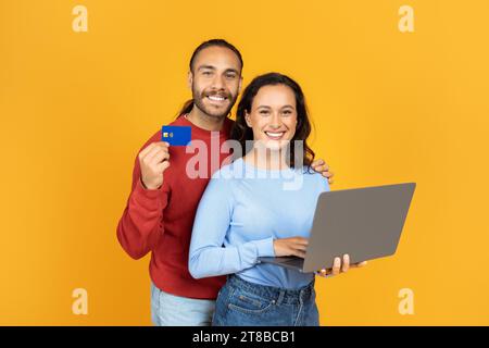 Positives Millennial-Paar, das Laptop benutzt und Bankkreditkarte zeigt Stockfoto