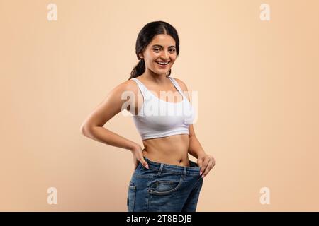 Happy Young Indian Woman Trägt Übergroße Jeans, Die Das Ergebnis Von Gewichtsverlust Demonstrieren Stockfoto