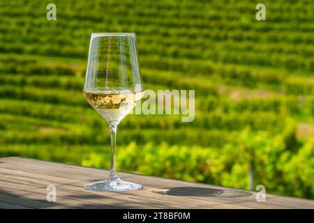 Nahaufnahme von Weißwein in einem Glas auf einem Holztisch, umgeben von grünen Weinbergen Stockfoto