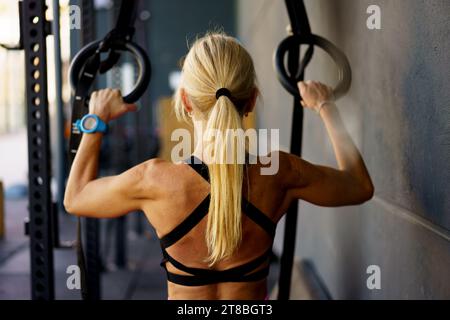 Kräftig sitzende junge Frau, die im Fitnessstudio mit Turnerringen trainiert Stockfoto