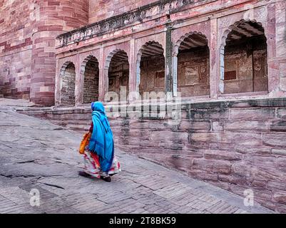 JODHPUR, INDIEN - 30. DEZEMBER 2022: Eine anonyme Frau in einem farbenfrohen Sari geht die Rampe hinauf zu den Toren des Mehrangarh-Forts in Jodhpur. Stockfoto