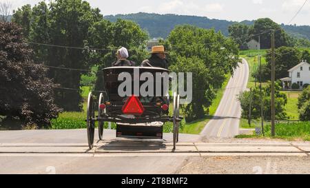 Ronks, Pennsylvania, 23. Juli 2023 - Rückansicht eines amischen Paares in einem offenen Pferd und Buggy, Crossing RR Tracks auf der Rural Road Stockfoto