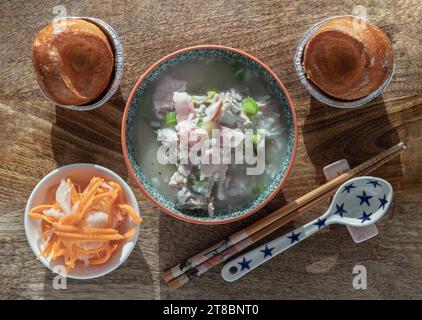 Heißer gekochter Reis oder Reisbrei mit Schweinerippchen Suppe und Schinken serviert mit frittiertem Teig, eingelegter Karotte und Rettich auf hölzernem Schneidebrett. Er Stockfoto
