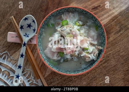 Heißer gekochter Reis oder Reisbrei mit Schweinerippchen Suppe und Schinken serviert mit Löffel und Essstäbchen auf Holztablett. Gesundes Frühstück, Blick von oben, Stockfoto