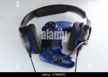 Ein Foto von einem dunkelblauen PlayStation-Spielekonsolen-Controller und zwei Kopfhörern auf einem weißen Tisch. Gamer. Stockfoto