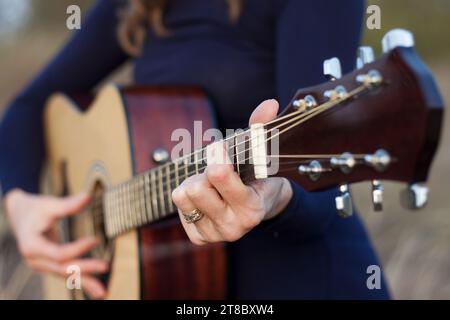 Nahaufnahme von Frauenhänden, die eine Akustikgitarre spielen. Freizeit im Freien, kreativer Abend, warmer Herbst, Sonnenuntergang. Romantische Stimmung. Selektiver Fokus Stockfoto