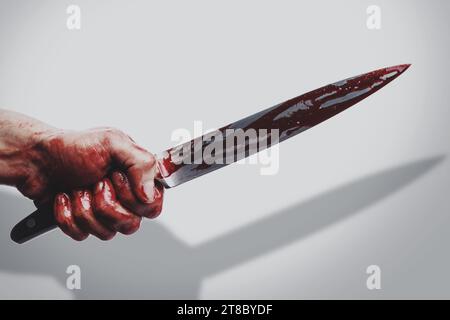Männliche Hand mit einem Messer in Blutflecken, der Schatten auf weißem Hintergrund wirft Stockfoto