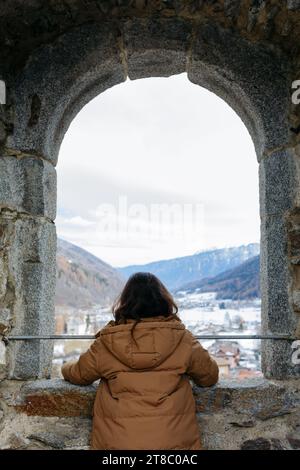 Rückansicht eines stehenden Mädchens, das schneebedeckte Berge vom großen Fenster aus beobachtet Stockfoto