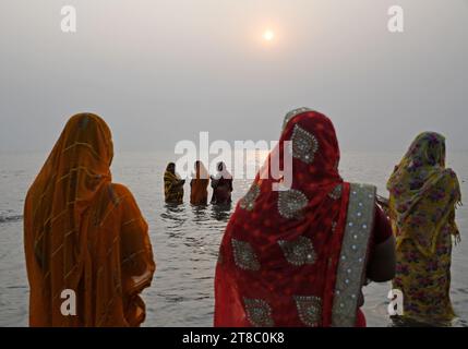 Hindufrauen, die im Wasser stehen, beten zur untergehenden Sonne anlässlich von Chhath Puja am Strand in Mumbai. Chhath Puja wird von den Menschen aus den nordstaaten Indiens gefeiert. Die Gläubigen versammeln sich in der Nähe eines Wasserkörpers, führen Rituale durch und beten zur untergehenden Sonne am Abend und zur aufgehenden Sonne. Am nächsten Morgen danken sie ihm für das Leben auf der Erde. Stockfoto