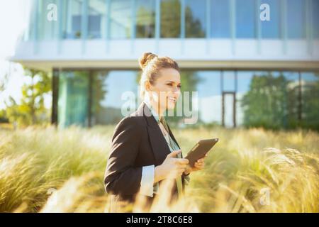 Lächelnde moderne Arbeitnehmerin im Geschäftsviertel in schwarzer Jacke mit Tablet-PC. Stockfoto