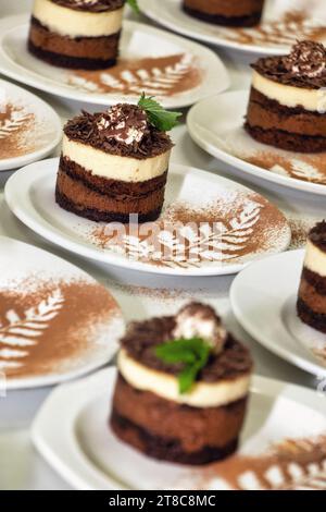 Schokoladen- und Cappuccino-Mini-Kuchen auf kleinen weißen Tellern Kakaoblätter garnieren Stockfoto