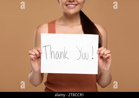 Frau, die Karte mit Phrase hält Danke auf braunem Hintergrund, Nahaufnahme Stockfoto