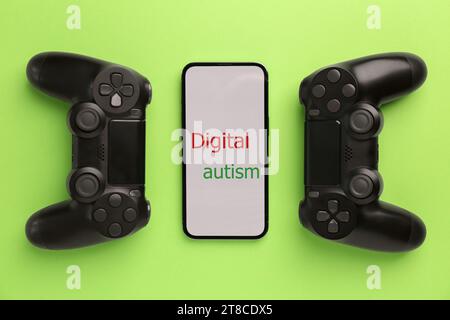 Smartphone mit Phrase Digital Autism und Gamepads auf hellgrünem Hintergrund, flache Lay. Suchtverhalten Stockfoto