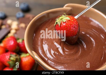 Frische Erdbeere in Fonduetopf mit geschmolzener Schokolade am Tisch, Nahaufnahme Stockfoto