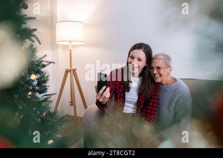 Feiern Sie Weihnachten, Silvester, Mutter und Tochter halten ein Smartphone-Selfie und machen Sie Fotos, grüßen Sie während der sozialen Distanz per Videoanruf Stockfoto