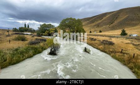 Überfluteter Bach auf der kurvenreichen Schotterstraße zwischen Lake Tekapo und Lake Pukaki in ländlichem Ackerland Stockfoto