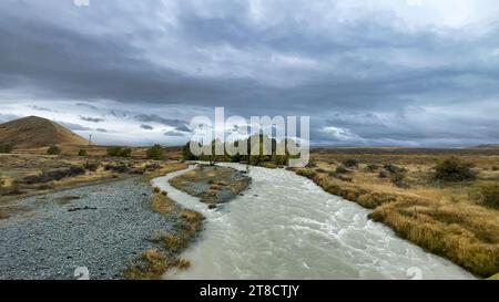 Überfluteter Bach auf der kurvenreichen Schotterstraße zwischen Lake Tekapo und Lake Pukaki in ländlichem Ackerland Stockfoto