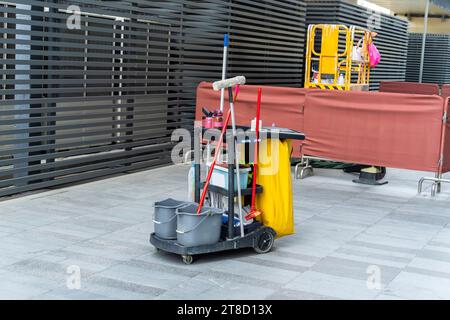 Reinigungswagen an einem öffentlichen Ort mit Reinigungsprodukten: Mopp, Eimer zur Bodenreinigung, Besenlöffel, Haushaltschemikalien, Haushaltslappen Stockfoto