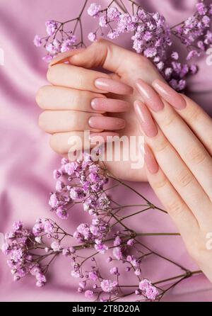 Weibliche Hände mit schöner Maniküre mit Gipsofila-Blüten auf rosa Seide Stockfoto