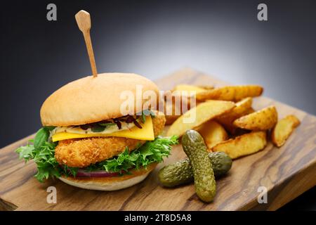 Hausgemachter Fischburger mit Käse, Gemüse und Tatarsauce auf einem hölzernen Schneidebrett. Stockfoto