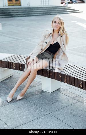Eine Frau im Regenmantel auf einem Spaziergang sitzt auf einer Bank Stockfoto
