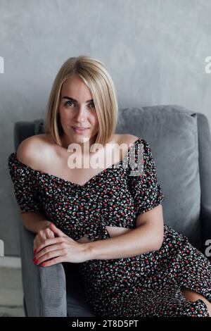 Blonde in bunten Kleidern liegt drinnen auf einem Stuhl Stockfoto