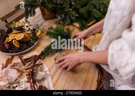 Draufsicht Komposition weiblicher Hände, die Weihnachtskranz aus natürlichen Zweigen von Fichte, Kiefer, Eukalyptus herstellen. Das Mädchen wickelt grüne Zweige auf die Kraft-Basis Stockfoto