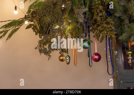 Authentisches, kreatives botanisches Weihnachtsdesign im rustikalen Stil. Hängende Girlande aus grünen Tannenzweigen mit Weihnachtskugeln an Bändern. Helles Vintage-G Stockfoto