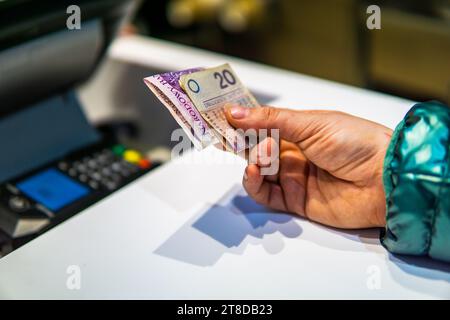 Frau, die in polnischem Zloty pln für eine Mahlzeit neben dem Inflationskonzept der Kasse Polski ład bezahlt Stockfoto