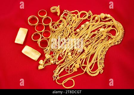 Viele goldene Ketten und Goldbarren auf rotem Samthintergrund. Stockfoto