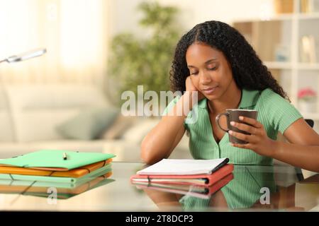 Schwarzer Student, der Notizen auswendig macht und Kaffee zu Hause hält Stockfoto