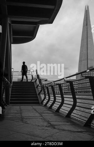 Schwarz-weiß-Bild der Silhouette eines Mannes, der über die Außentreppen geht, mit Londons Symbol, The Shard im Hintergrund. Stockfoto