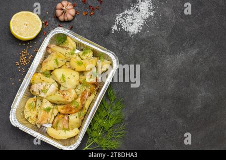 Gebackene Kartoffeln in Folie mit Dill. Rosmarin und grüne Paprika, Knoblauch und Zitrone auf dem Tisch. Schwarzer Hintergrund. Flache Lagen. Kopierbereich Stockfoto