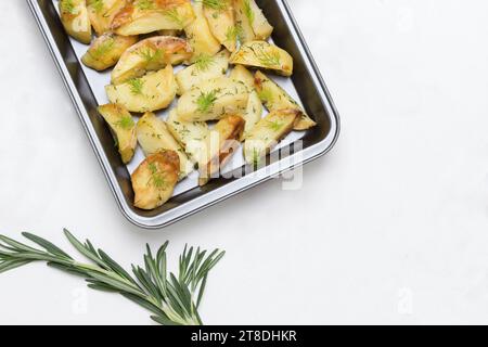 Gebackene Kartoffeln in der Auflaufform. Rosmarin und Paprika auf dem Tisch. Weißer Hintergrund. Flache Lagen. Kopierbereich Stockfoto