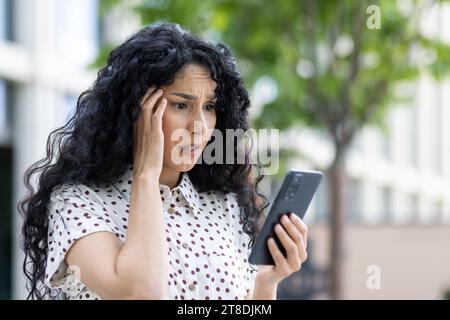 Traurig enttäuschte Frau erhielt Online-Benachrichtigung mit schlechten Nachrichten auf ihrem Telefon, Geschäftsfrau ging außerhalb des Bürogebäudes, benutzte Anwendung auf dem Smartphone, las soziale Medien unzufrieden. Stockfoto