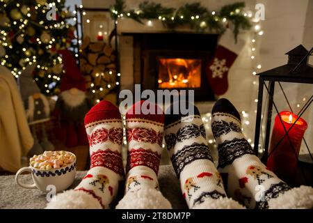 Paare genießen am warmen Kamin und wärmen ihre Füße in Wollsocken mit Weihnachtsschmuck und Weihnachtsbaum und Dekorationshintergrund auf. Gemütlicher Winter, Weihnachten und Familie. Stockfoto