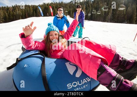 Eltern schieben ein junges Mädchen in einem Skigebiet auf eine Tube. Stockfoto